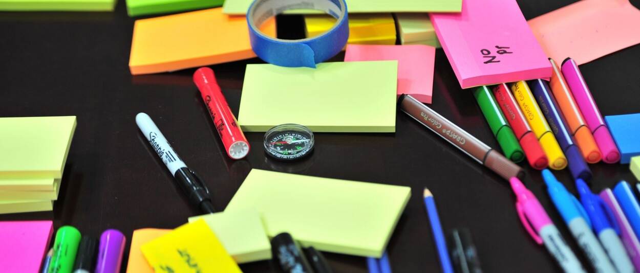 A black desk on whiche are spread many coloured post-its, markers and in the middle is a small compass
