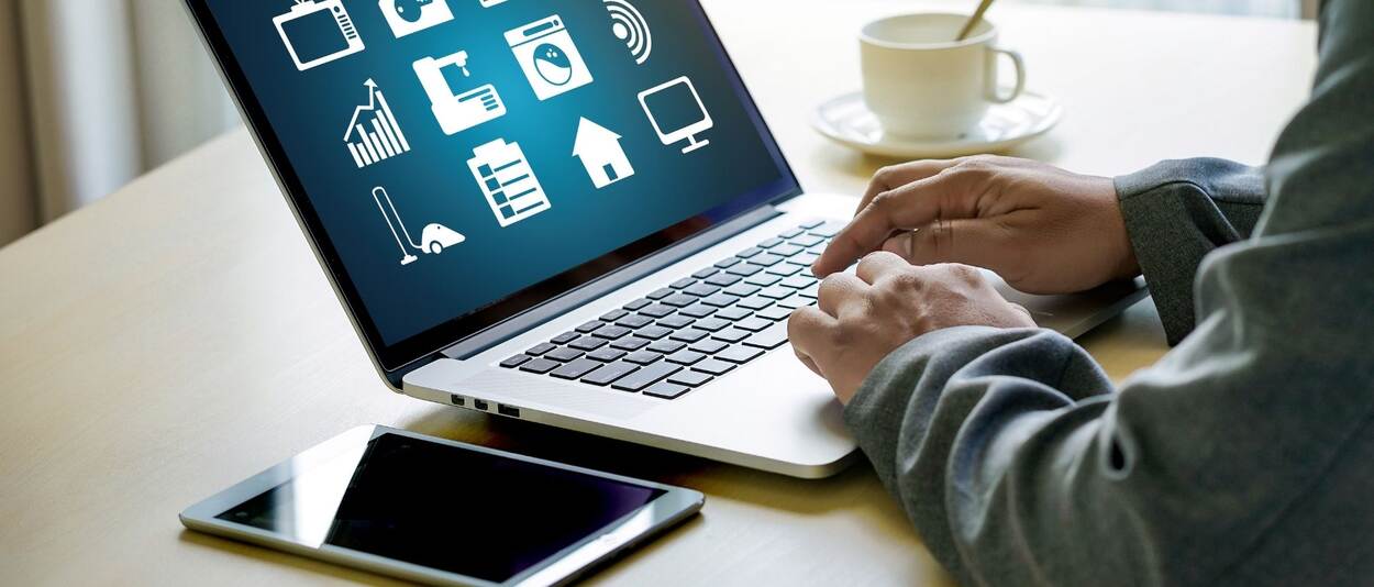 A desk with a laptop where you see two hands typing on the keyboard