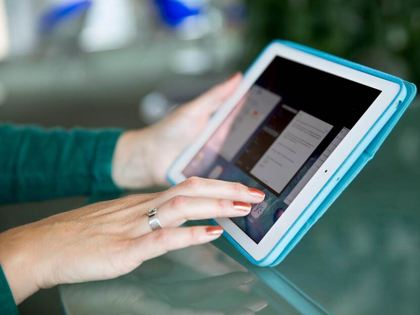 A hand, of which the nails are painted red, is touching the screen of an iPad